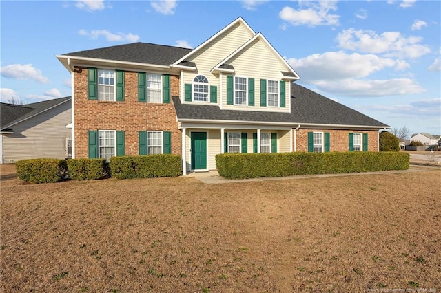 view of front of home with roof with shingles, a front yard, and brick siding