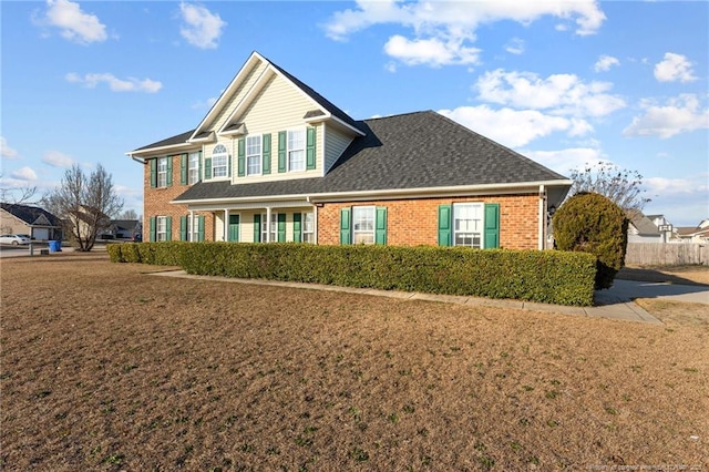 view of front of property with brick siding, a front lawn, and a shingled roof