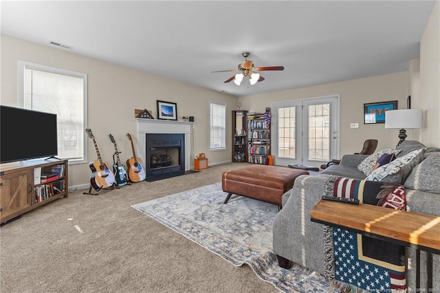 living room featuring carpet, visible vents, a fireplace with flush hearth, ceiling fan, and baseboards