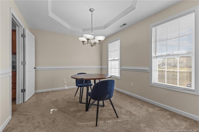 carpeted dining room with a notable chandelier, visible vents, baseboards, ornamental molding, and a tray ceiling