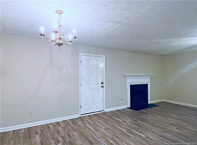 unfurnished living room featuring a fireplace with flush hearth, baseboards, wood finished floors, and an inviting chandelier