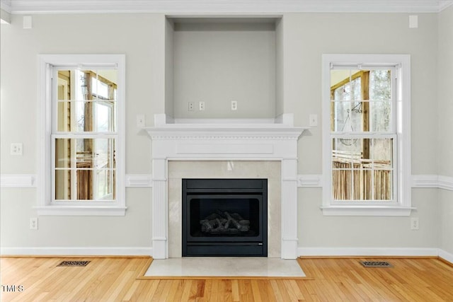 unfurnished living room with wood finished floors, a fireplace with flush hearth, baseboards, visible vents, and crown molding