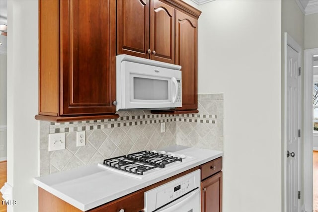 kitchen featuring brown cabinets, crown molding, light countertops, decorative backsplash, and white appliances