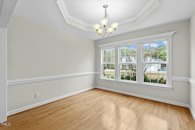 empty room with baseboards, ornamental molding, a tray ceiling, light wood-type flooring, and a notable chandelier