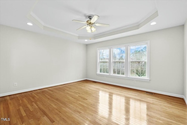 spare room with visible vents, baseboards, a raised ceiling, ornamental molding, and light wood-style floors