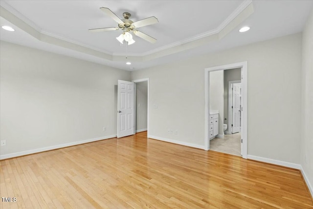 empty room with light wood-type flooring, a raised ceiling, and baseboards