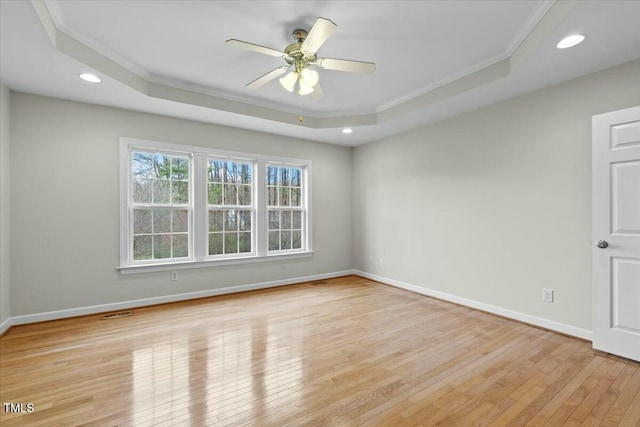 empty room with recessed lighting, baseboards, light wood finished floors, a raised ceiling, and crown molding