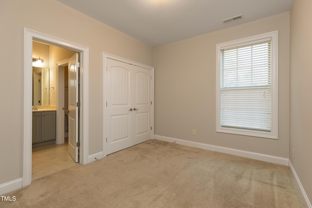 unfurnished bedroom featuring visible vents, baseboards, a closet, ensuite bathroom, and light colored carpet