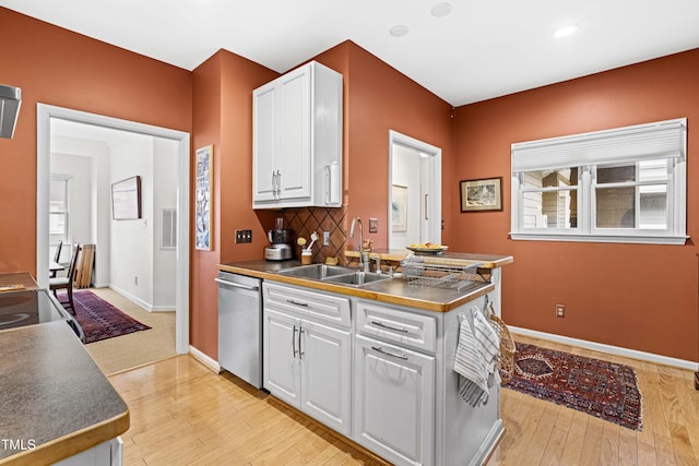 kitchen featuring tasteful backsplash, white cabinets, stainless steel dishwasher, light wood-style floors, and a sink