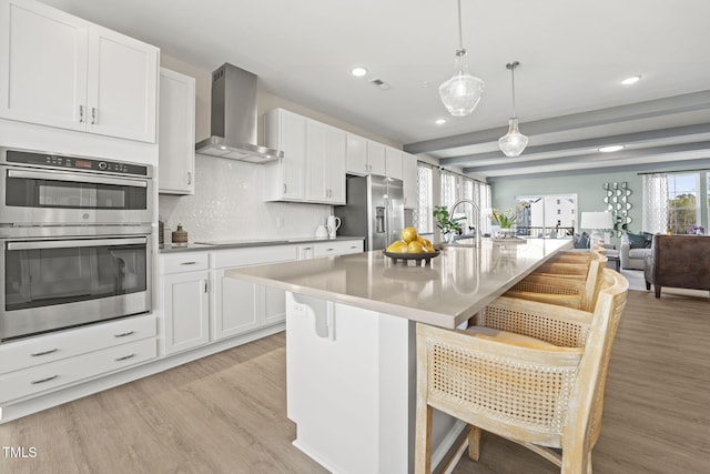 kitchen with a breakfast bar, pendant lighting, stainless steel appliances, open floor plan, and wall chimney range hood