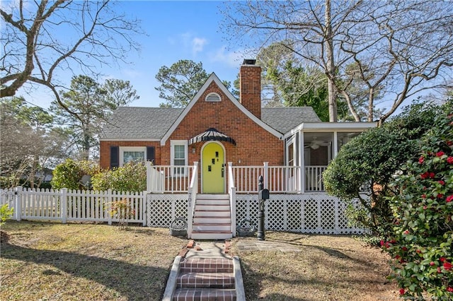 tudor house with a shingled roof, a sunroom, a chimney, fence, and brick siding