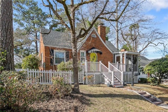 english style home with a sunroom, a chimney, roof with shingles, fence, and brick siding