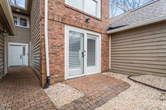 doorway to property with a shingled roof, brick siding, and a patio