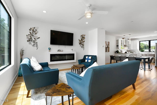 living room featuring light wood finished floors, recessed lighting, baseboards, and a glass covered fireplace