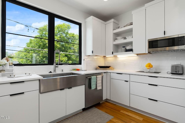 kitchen with open shelves, light countertops, decorative backsplash, appliances with stainless steel finishes, and a sink