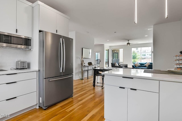 kitchen with tasteful backsplash, light countertops, appliances with stainless steel finishes, white cabinets, and light wood-type flooring