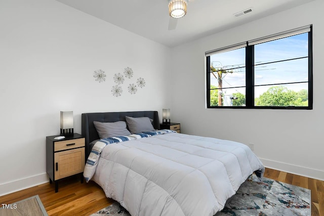 bedroom with baseboards, visible vents, and wood finished floors