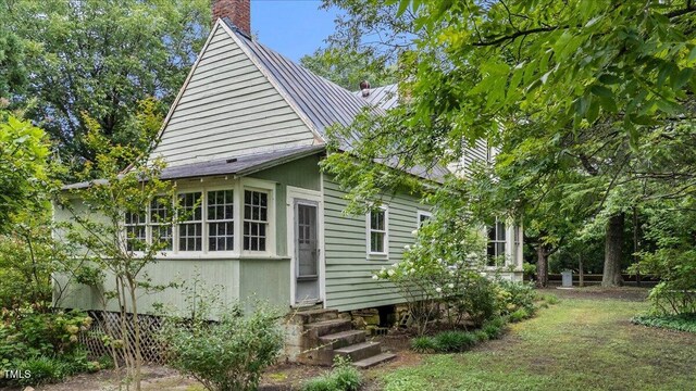 view of property exterior featuring entry steps, a chimney, and metal roof