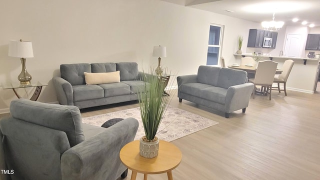 living area featuring light wood finished floors, baseboards, and a chandelier