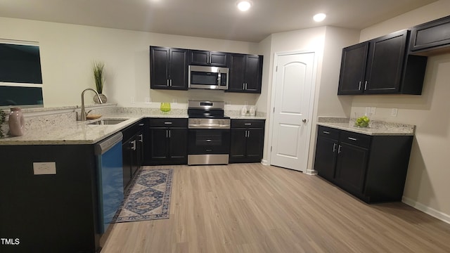 kitchen with light wood finished floors, a peninsula, stainless steel appliances, dark cabinetry, and a sink