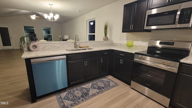 kitchen featuring stainless steel appliances, a sink, a peninsula, and light stone counters