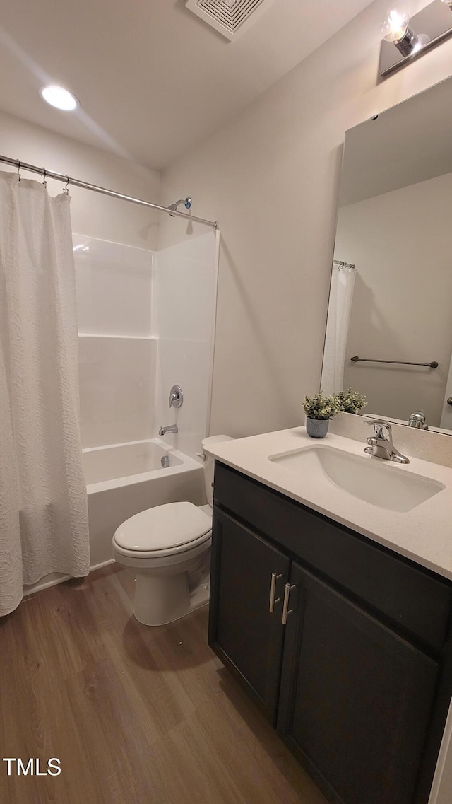 bathroom featuring visible vents, shower / bathtub combination with curtain, toilet, vanity, and wood finished floors