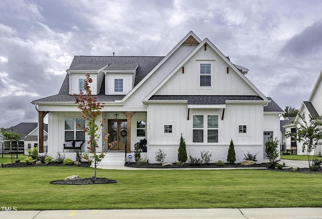 modern farmhouse style home featuring covered porch, a shingled roof, board and batten siding, and a front yard