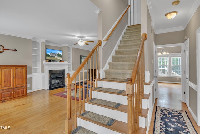 staircase with built in shelves, a fireplace with flush hearth, wood finished floors, baseboards, and crown molding