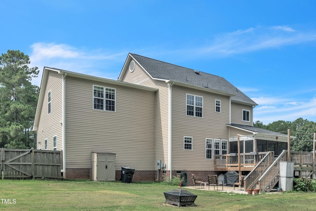 rear view of property with a lawn, stairway, a sunroom, a deck, and a fire pit