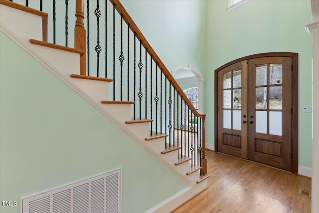 entryway with arched walkways, light wood-style flooring, visible vents, baseboards, and french doors