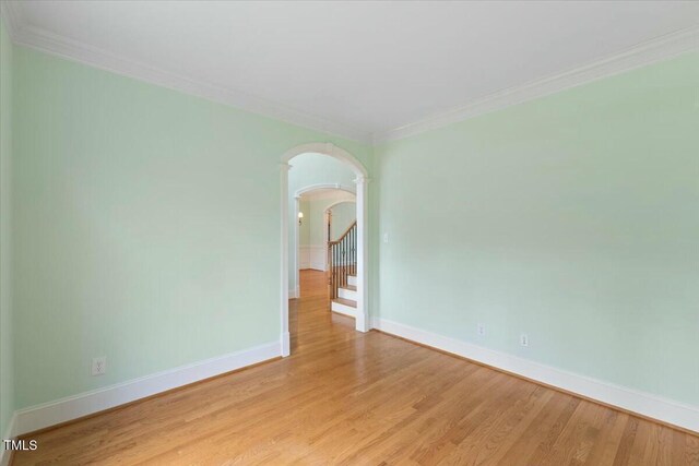 empty room featuring arched walkways, crown molding, light wood-type flooring, and baseboards