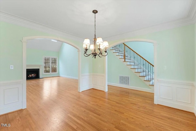 unfurnished dining area featuring visible vents, stairs, arched walkways, and a lit fireplace