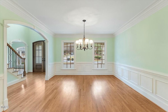 unfurnished dining area with arched walkways, crown molding, light wood-style flooring, a chandelier, and stairs