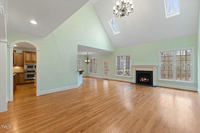 unfurnished living room featuring high vaulted ceiling, light wood-style flooring, a fireplace with flush hearth, baseboards, and an inviting chandelier