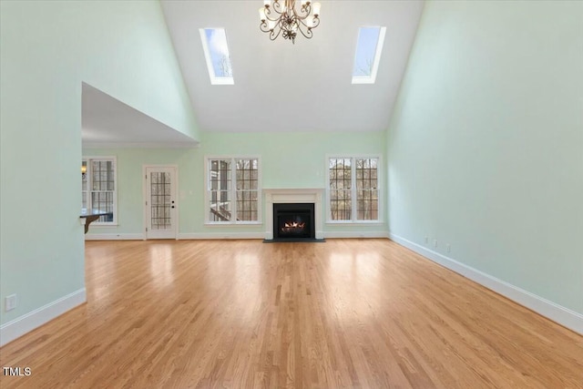 unfurnished living room featuring light wood finished floors, a skylight, a fireplace with flush hearth, and baseboards