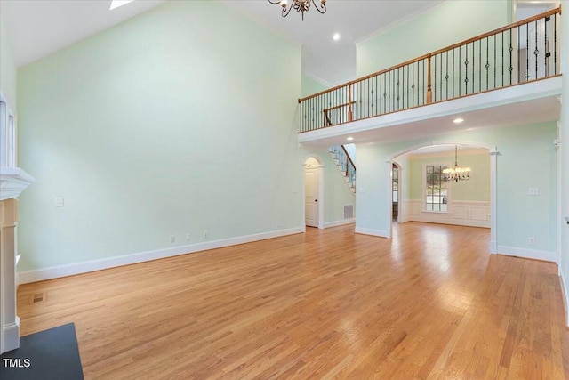 unfurnished living room with arched walkways, a towering ceiling, an inviting chandelier, light wood-type flooring, and baseboards