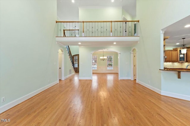 unfurnished living room with light wood-type flooring, baseboards, a towering ceiling, and arched walkways