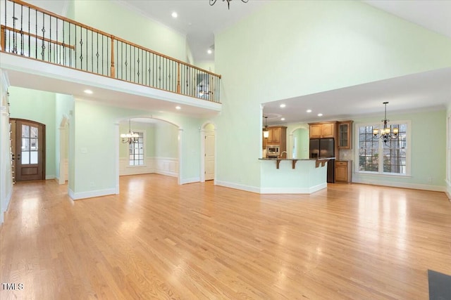 unfurnished living room with light wood-type flooring, arched walkways, a notable chandelier, and baseboards