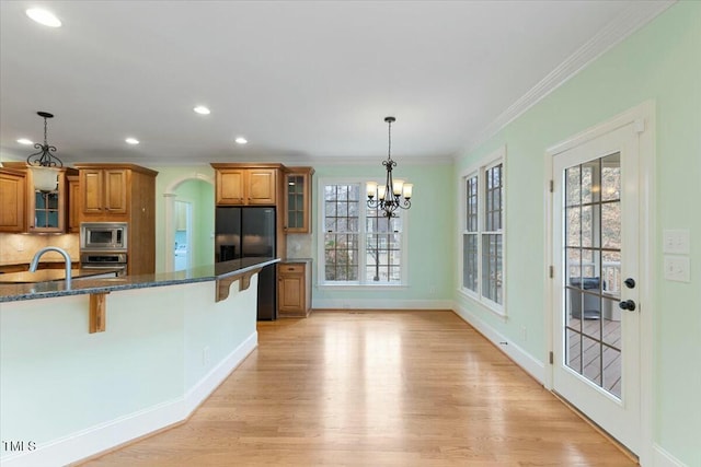 kitchen featuring appliances with stainless steel finishes, brown cabinetry, glass insert cabinets, and hanging light fixtures