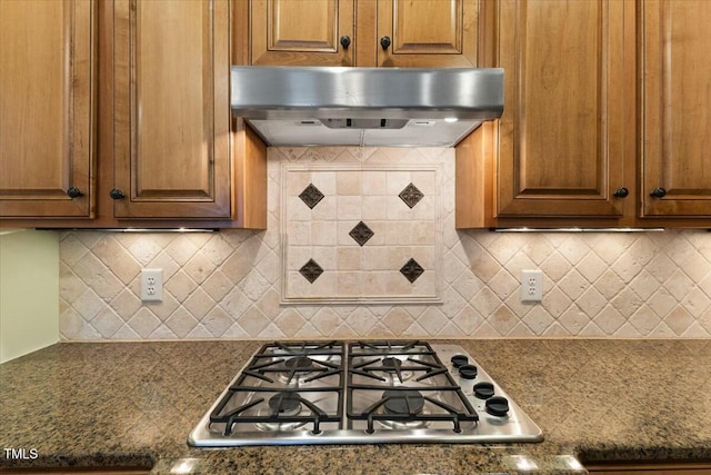 kitchen featuring under cabinet range hood, gas stovetop, brown cabinetry, and decorative backsplash