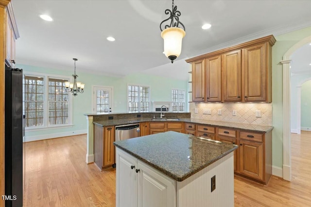 kitchen featuring arched walkways, brown cabinets, hanging light fixtures, a sink, and a peninsula