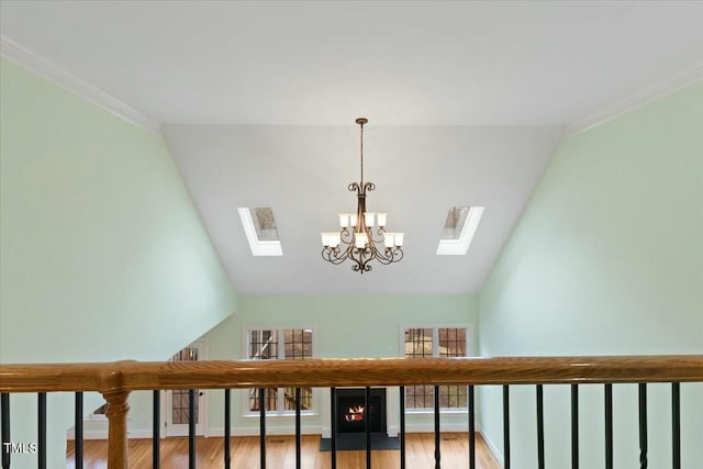 stairs with a skylight, wood finished floors, baseboards, ornamental molding, and an inviting chandelier