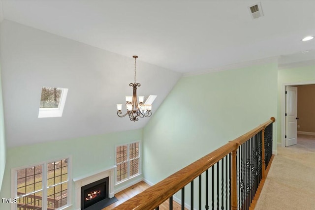 hallway with baseboards, visible vents, light colored carpet, lofted ceiling with skylight, and a chandelier