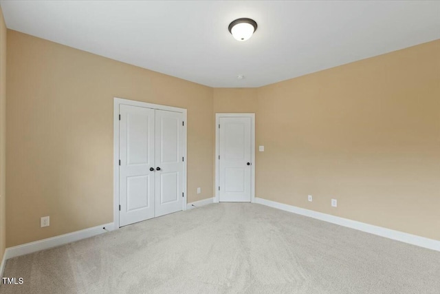 unfurnished bedroom featuring baseboards, a closet, and light colored carpet