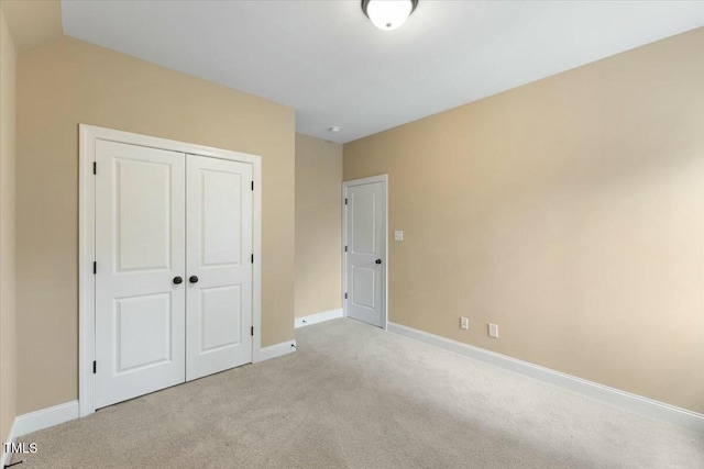 unfurnished bedroom with light carpet, a closet, and baseboards