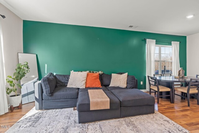 living room featuring an accent wall, visible vents, and wood finished floors