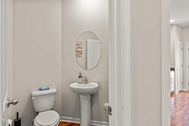 half bathroom featuring baseboards, toilet, and wood finished floors