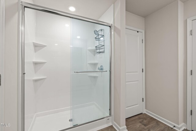 full bath featuring a shower stall, baseboards, and wood finished floors