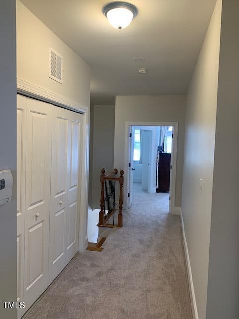 hall with carpet floors, baseboards, visible vents, and an upstairs landing