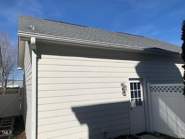 view of side of property featuring roof with shingles and fence